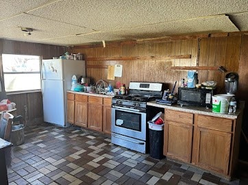 kitchen with dark tile floors, wood walls, stainless steel gas range oven, and white refrigerator