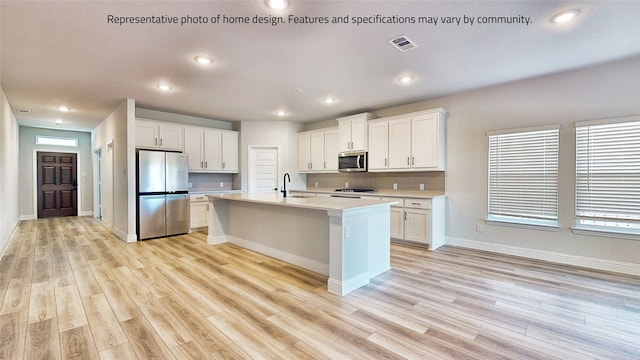 kitchen featuring light hardwood / wood-style flooring, an island with sink, stainless steel appliances, sink, and white cabinets