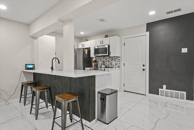 kitchen featuring white cabinetry, a kitchen breakfast bar, stainless steel appliances, backsplash, and light tile floors