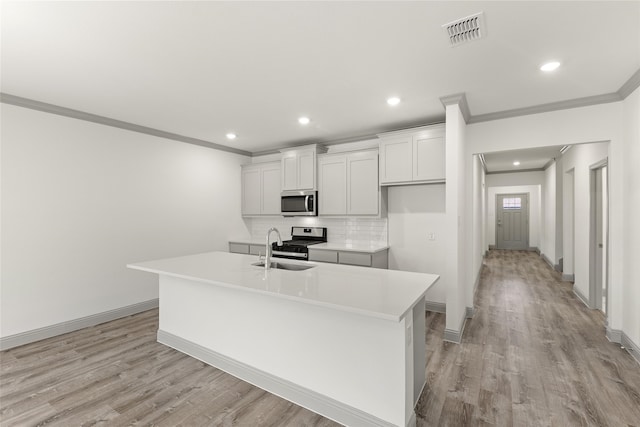 kitchen with light wood-type flooring, stainless steel appliances, a kitchen island with sink, and sink