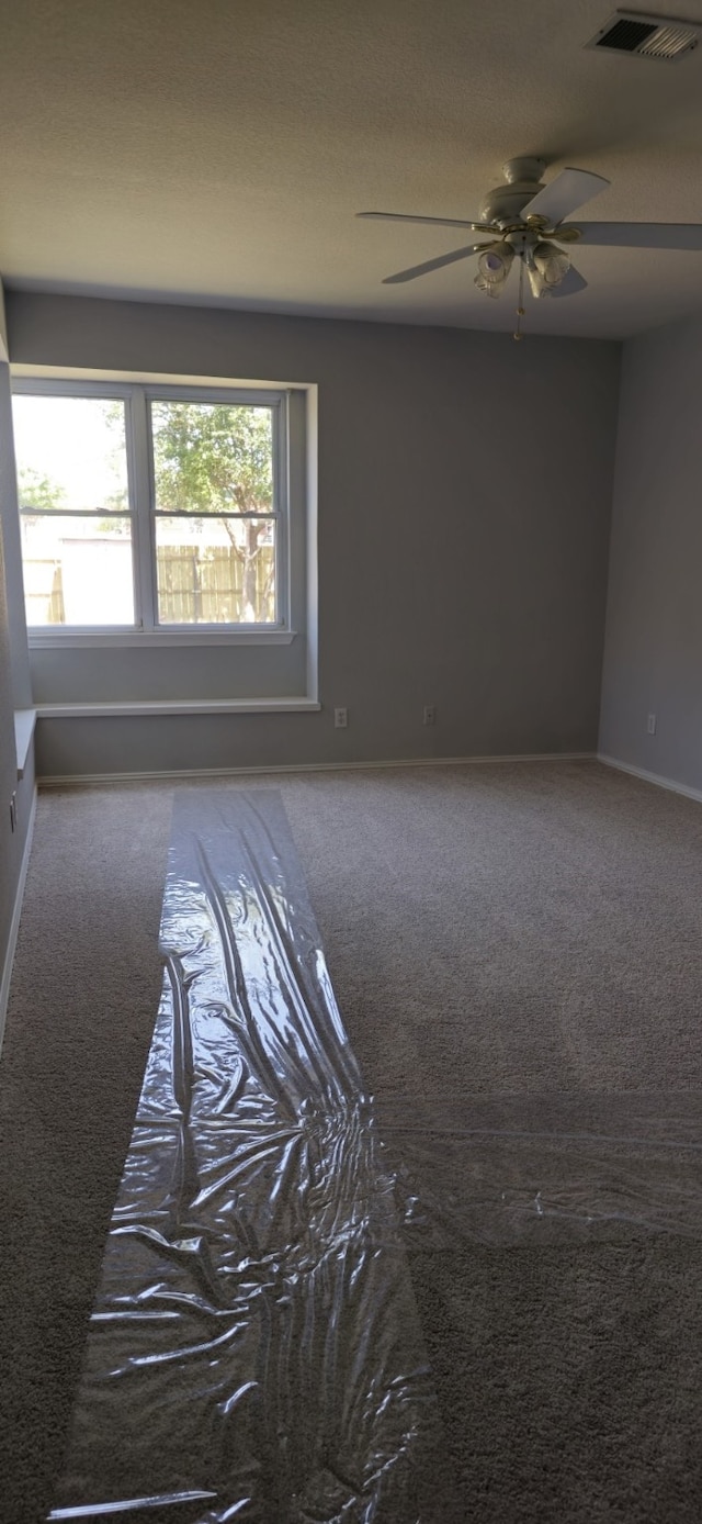 empty room featuring carpet floors, a ceiling fan, visible vents, and baseboards