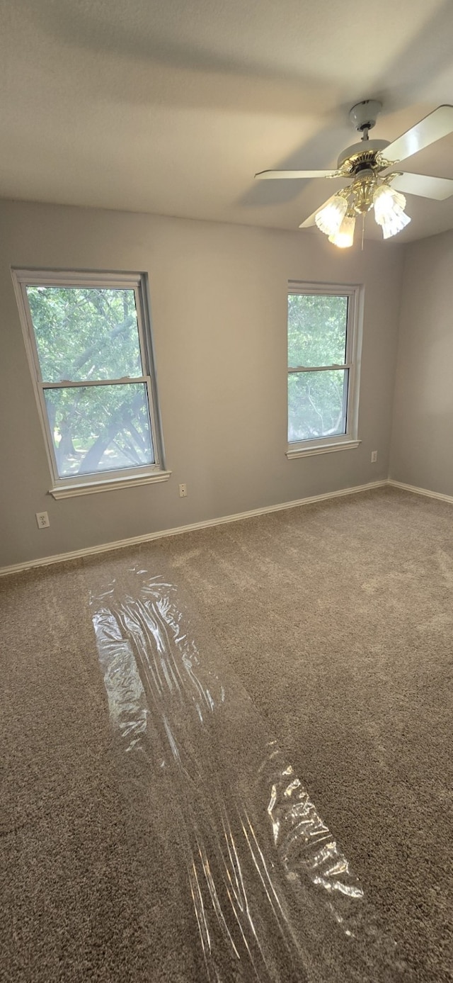 spare room featuring a healthy amount of sunlight, carpet floors, ceiling fan, and baseboards