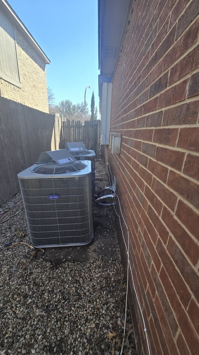 exterior details featuring fence, central AC unit, and brick siding