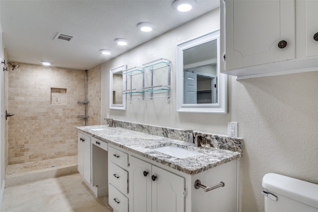 bathroom with a tile shower, vanity, and toilet