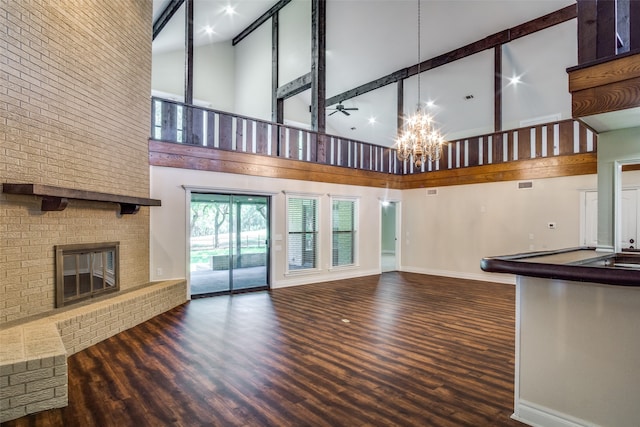 unfurnished living room featuring ceiling fan with notable chandelier, dark hardwood / wood-style floors, a high ceiling, and a brick fireplace