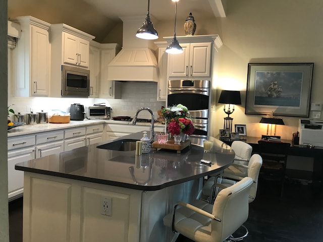 kitchen featuring a kitchen bar, stainless steel appliances, a kitchen island with sink, decorative light fixtures, and white cabinets