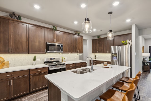 kitchen featuring pendant lighting, stainless steel appliances, sink, a kitchen island with sink, and dark brown cabinets