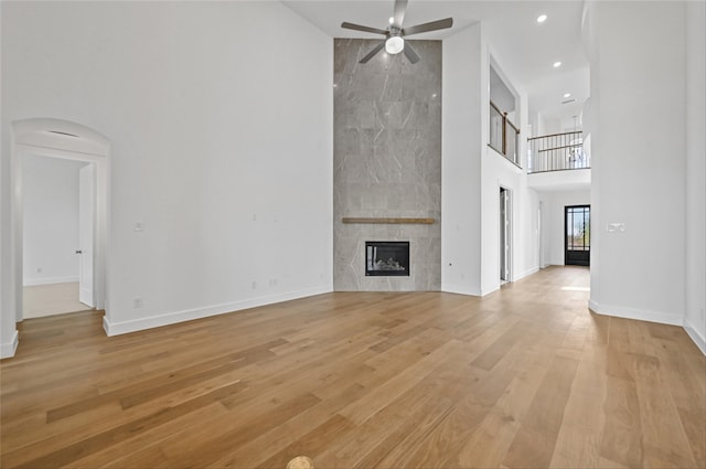 unfurnished living room featuring a high ceiling, light wood-type flooring, a tiled fireplace, and ceiling fan