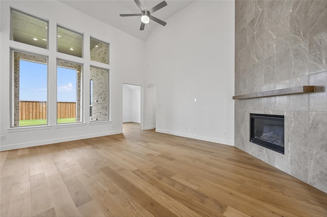 unfurnished living room featuring high vaulted ceiling, light hardwood / wood-style flooring, ceiling fan, and a tile fireplace