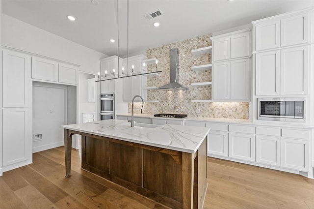 kitchen with light hardwood / wood-style floors, white cabinets, sink, a kitchen island with sink, and wall chimney range hood