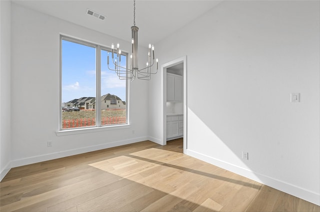 unfurnished dining area with light wood-type flooring, a wealth of natural light, and a notable chandelier