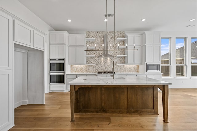 kitchen featuring a kitchen island with sink, light hardwood / wood-style flooring, white cabinetry, and light stone counters