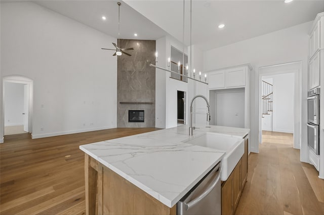 kitchen with stainless steel appliances, white cabinetry, a center island with sink, light stone counters, and decorative light fixtures