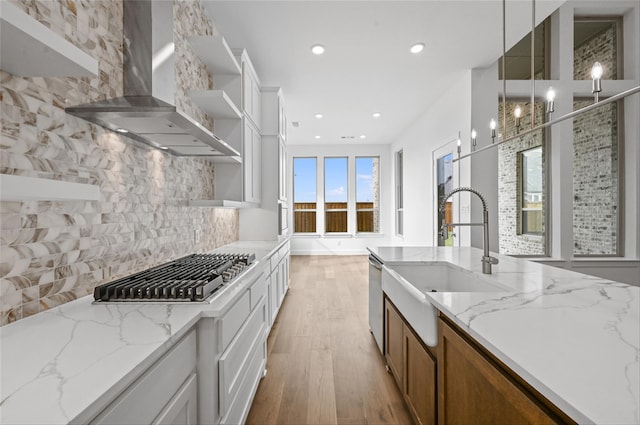 kitchen with white cabinetry, decorative light fixtures, light stone countertops, and wall chimney range hood