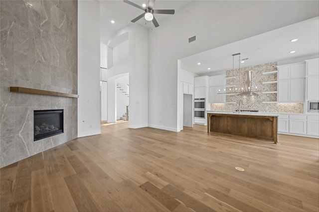 unfurnished living room featuring a fireplace, light wood-type flooring, ceiling fan, and a towering ceiling