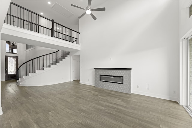 unfurnished living room with ceiling fan, a wealth of natural light, wood-type flooring, and a towering ceiling