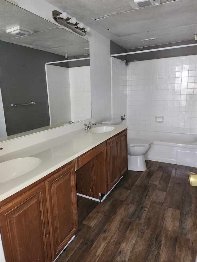 full bathroom with dual bowl vanity, hardwood / wood-style floors, toilet, and tiled shower / bath