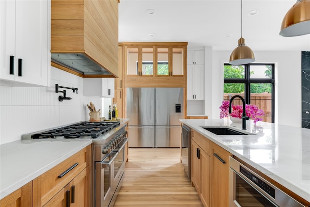 kitchen with custom exhaust hood, white cabinets, appliances with stainless steel finishes, pendant lighting, and light stone counters