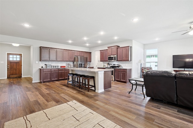 kitchen featuring a kitchen bar, stainless steel appliances, a kitchen island, ceiling fan, and wood-type flooring