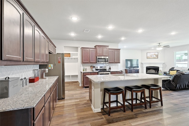 kitchen featuring hardwood / wood-style flooring, tasteful backsplash, light stone counters, and appliances with stainless steel finishes