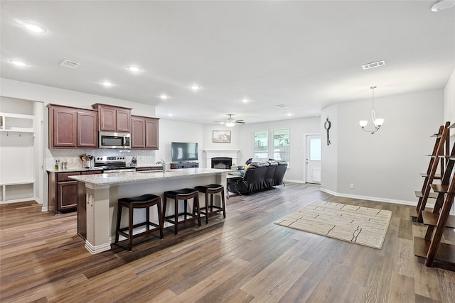 kitchen with appliances with stainless steel finishes, a center island with sink, a breakfast bar, ceiling fan with notable chandelier, and wood-type flooring