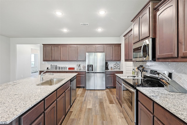 kitchen with backsplash, light stone countertops, light wood-type flooring, and stainless steel appliances