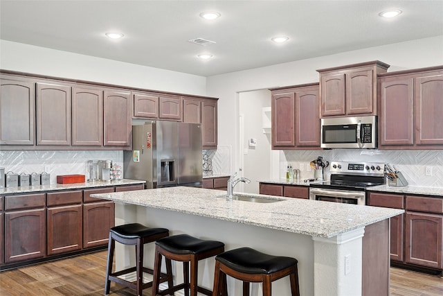 kitchen with backsplash, light stone counters, an island with sink, appliances with stainless steel finishes, and sink