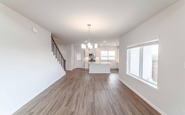 unfurnished living room with a chandelier, wood finished floors, baseboards, and stairs