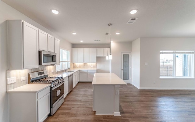 kitchen with stainless steel appliances, a sink, tasteful backsplash, wood finished floors, and a kitchen island
