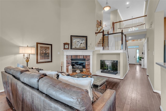 living room featuring a brick fireplace, a high ceiling, and dark wood-type flooring