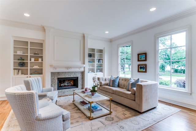 living room with built in shelves, a high end fireplace, light hardwood / wood-style floors, and crown molding