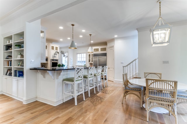 kitchen with light hardwood / wood-style floors, stainless steel appliances, white cabinets, kitchen peninsula, and decorative light fixtures