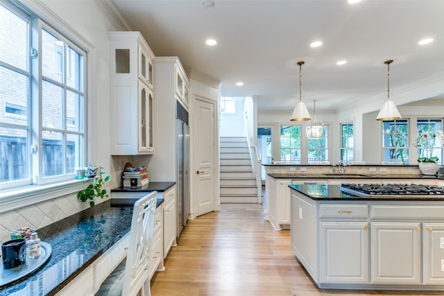 kitchen featuring light hardwood / wood-style floors, tasteful backsplash, hanging light fixtures, stainless steel gas cooktop, and white cabinetry