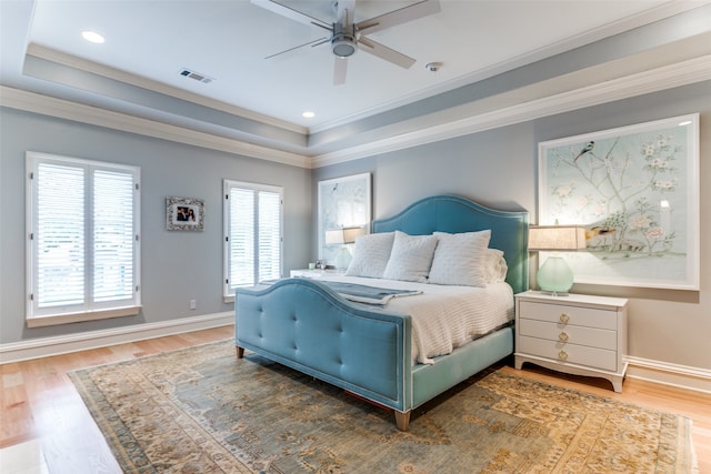 bedroom with a tray ceiling, ornamental molding, ceiling fan, and hardwood / wood-style floors