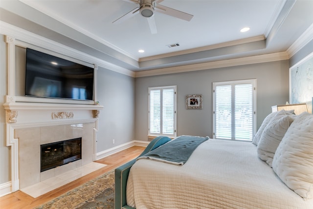 bedroom with ceiling fan, a tray ceiling, hardwood / wood-style floors, ornamental molding, and a tile fireplace