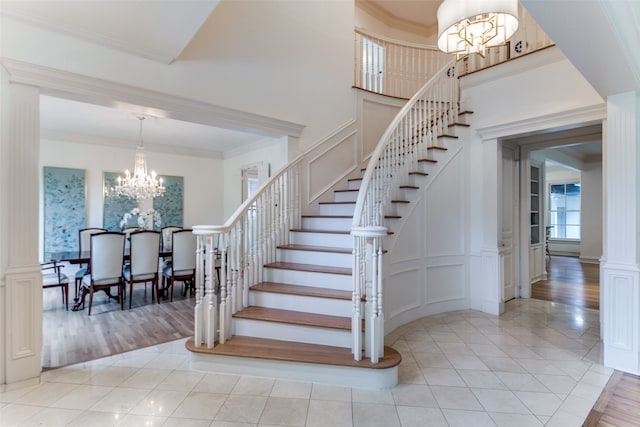 stairway featuring a notable chandelier, a high ceiling, ornamental molding, and light hardwood / wood-style floors