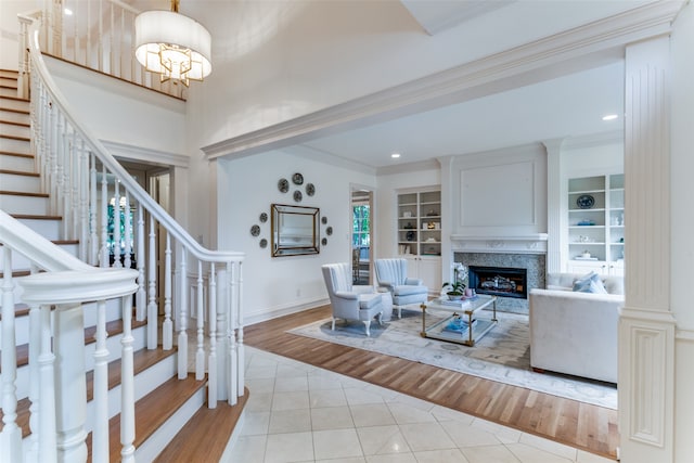 living room featuring a chandelier, light tile flooring, built in features, ornamental molding, and a high end fireplace