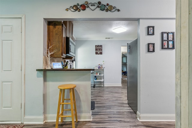 kitchen featuring kitchen peninsula, a textured ceiling, appliances with stainless steel finishes, dark hardwood / wood-style floors, and a kitchen bar