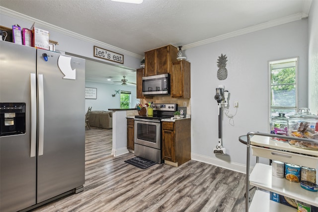 kitchen with appliances with stainless steel finishes, a textured ceiling, crown molding, ceiling fan, and hardwood / wood-style floors