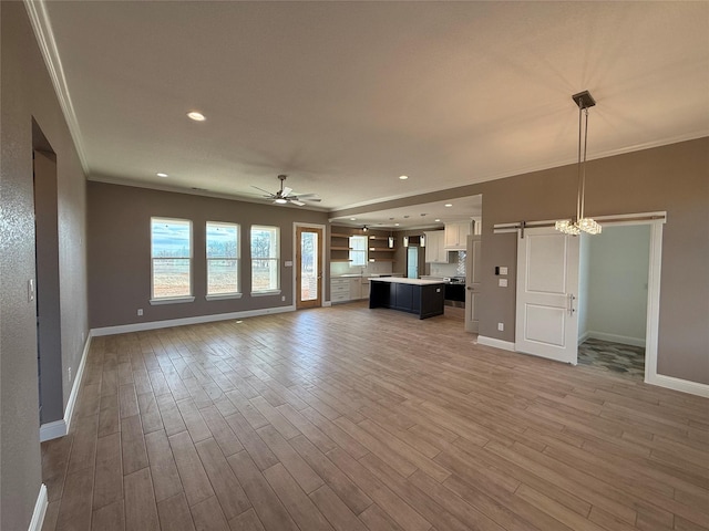 unfurnished living room with ceiling fan, wood-type flooring, a barn door, and ornamental molding