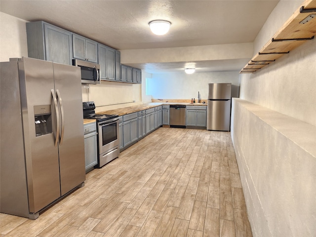 kitchen with light hardwood / wood-style floors, gray cabinetry, sink, appliances with stainless steel finishes, and a textured ceiling