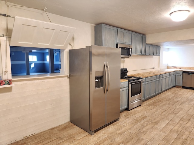 kitchen with appliances with stainless steel finishes, gray cabinetry, a textured ceiling, and light hardwood / wood-style flooring