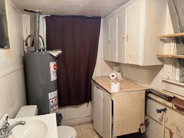 interior space with sink, light tile flooring, a textured ceiling, and gas water heater