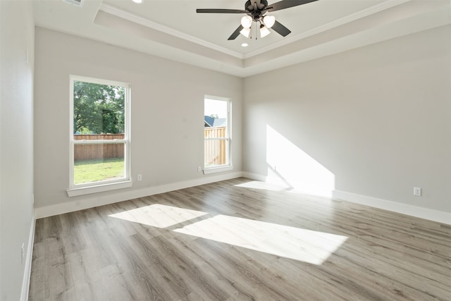 empty room with ornamental molding, light wood-type flooring, ceiling fan, and a raised ceiling