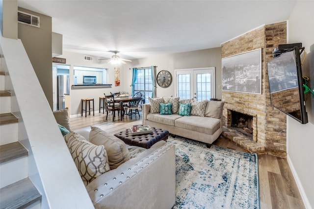 living room with brick wall, a fireplace, ceiling fan, wood-type flooring, and french doors