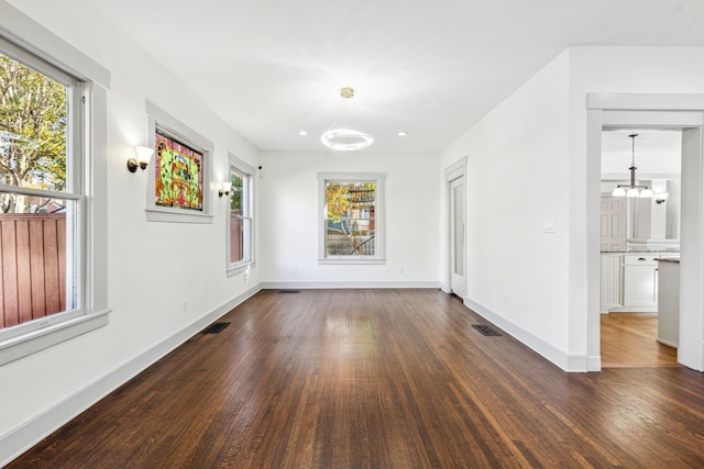 spare room featuring dark wood-type flooring and a chandelier