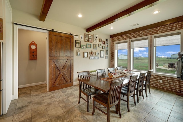 dining room with beam ceiling, a barn door, and brick wall