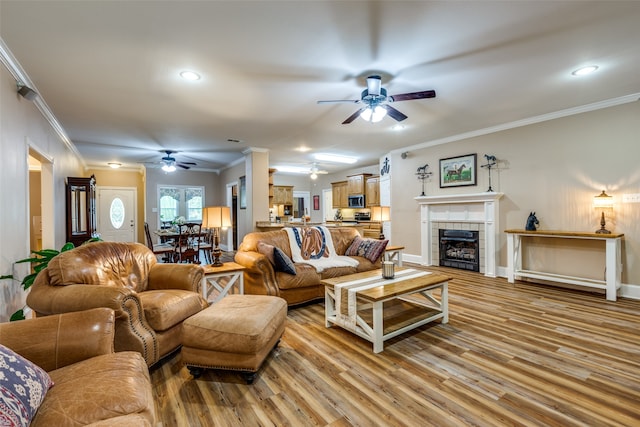 living room with ceiling fan, a tile fireplace, ornamental molding, and wood-type flooring