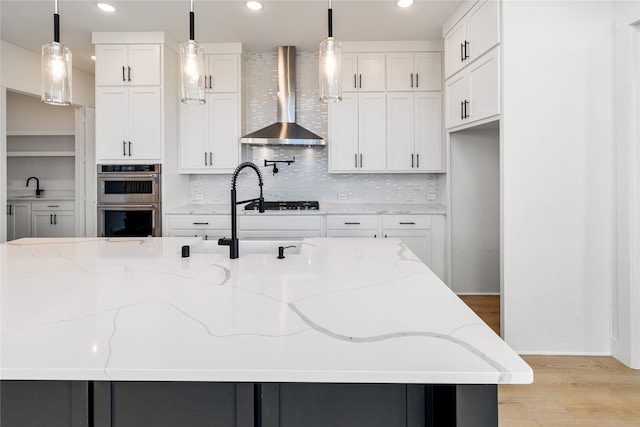 kitchen featuring light stone countertops, white cabinetry, hanging light fixtures, and wall chimney range hood