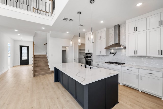 kitchen featuring white cabinets, a large island with sink, pendant lighting, and wall chimney exhaust hood